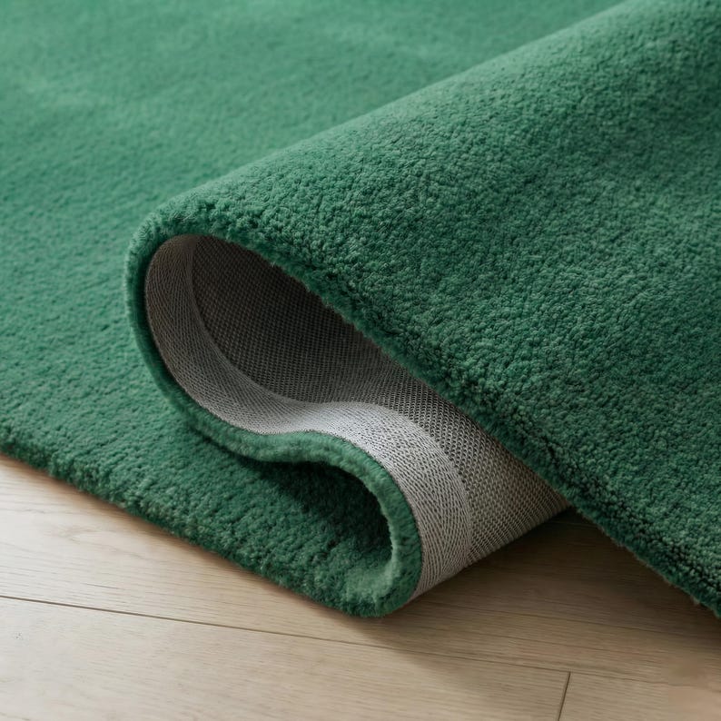 May include: A rolled-up, emerald green rug with a plush, textured surface. The underside reveals a gray, woven backing. The rug's edges are neatly finished, showcasing the quality of the material.