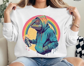 May include: White sweatshirt featuring a colorful illustration of a chameleon wearing a blue hoodie and holding a spray paint can. A rainbow and yellow circle are behind the chameleon. The text "PNG File - Digital Download Only (No Physical Item)" is at the bottom.