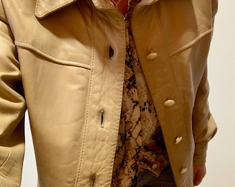Könnte beinhalten: Hellbraune Lederjacke mit Kragen und Knopfleiste. Die Jacke ist über einem gemusterten Hemd mit Knöpfen getragen. Die Jacke hat ein klassisches Design mit sichtbaren Nahtdetails. Der Gesamtstil ist Vintage.