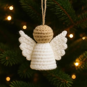 Puede incluir: Adorno navideño de ángel hecho a mano con ganchillo. El ángel tiene una cabeza beige, cuerpo y alas blancas, y una cuerda para colgar. El adorno está sobre un fondo borroso de árbol de Navidad con luces.