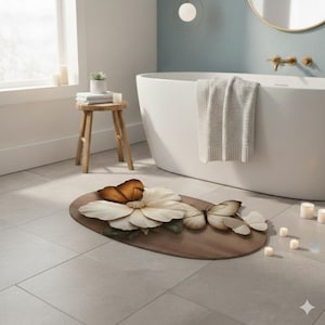 May include: Oval-shaped bath mat with a butterfly and flower design. The mat is brown with a large white flower and several butterflies in shades of brown and beige. The mat is placed on a tiled floor in a bathroom setting.