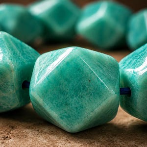 Pu&ograve; includere: Una collana di perline di amazzonite verde acqua sfaccettate e lucidate, infilate su un sottile cordino blu. Ogni perla presenta una forma geometrica a pi&ugrave; facce con una superficie liscia e lucida che riflette la luce, mostrando le sfumature.