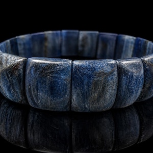Peut inclure: Un bracelet en kyanite bleue. Le bracelet est composé de pierres rectangulaires polies dans des tons de bleu et de gris. Les pierres sont assemblées pour former une boucle continue. Le bracelet est présenté sur une surface noire réfléchissante.