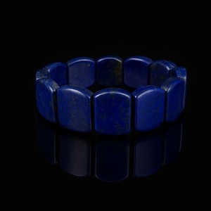 Op de afbeelding: Een donkerblauwe armband bestaande uit rechthoekige, gepolijste stenen. De stenen zijn diep, verzadigd blauw met subtiele kleurvariaties. De armband wordt getoond tegen een zwarte achtergrond, wat de kleur en vorm benadrukt.