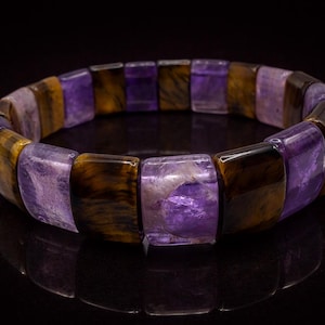 May include: A stretch bracelet featuring alternating rectangular beads of purple and brown tiger's eye stones. The bracelet is displayed on a black surface, reflecting the light.
