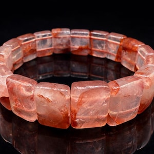 Op de afbeelding: Een armband gemaakt van rechthoekige, doorschijnende, rood-oranje stenen. De stenen zijn in een cirkelvormig patroon gerangschikt, tegen een donkere achtergrond. De armband is waarschijnlijk gemaakt van een natuurlijke edelsteen.