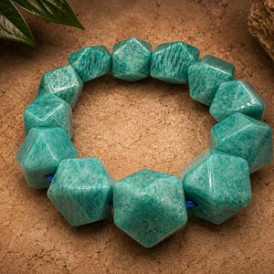 Pu&ograve; includere: Un braccialetto circolare composto da dodici perline geometriche sfaccettate di un vibrante colore verde acqua. Le perline sono infilate su un sottile cordino blu, creando un aspetto strutturato e angolare con una superficie liscia.