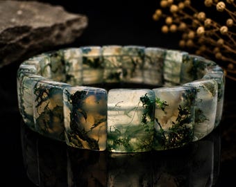 Può includere: Un bracciale composto da perline rettangolari in agata muschiata. Ogni perlina presenta una base traslucida bianco latte con distintive inclusioni dendritiche verde scuro a forma di felce che ricordano motivi di muschio.