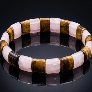 May include: A bracelet featuring alternating rectangular beads of pink quartz and tiger's eye. The bracelet is displayed on a reflective black surface, showcasing the natural colors and textures of the gemstones.