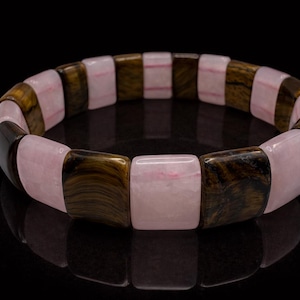 May include: A bracelet featuring alternating rectangular beads of pink and brown tiger eye stone. The bracelet is displayed on a black surface, showcasing its polished finish and natural color variations. The jewelry is a fashion accessory.