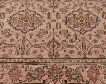 May include: A detailed close-up of a pink oriental rug with intricate geometric and floral patterns. The rug features a border with floral motifs in shades of pink, green, and brown, and a fringe along the bottom edge.