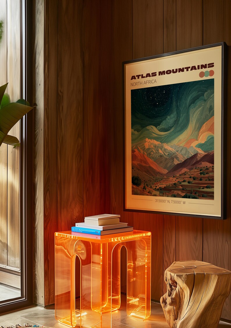 May include: A framed art print titled "Atlas Mountains North Africa" with a landscape scene of mountains and a starry sky. The print is displayed above a clear orange acrylic side table with books on top. A wooden stump is next to the table.