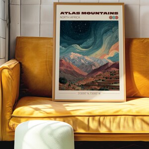 May include: A framed art print of the Atlas Mountains in North Africa. The artwork depicts a mountain range under a starry sky, with shades of blue, orange, and white. The print is displayed on a yellow sofa.