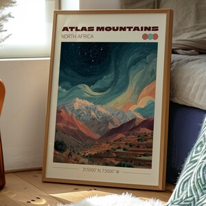 May include: Framed art print featuring a colorful landscape of the Atlas Mountains in North Africa. The artwork depicts a mountain range under a starry sky, with text that reads "Atlas Mountains North Africa" and coordinates. The frame is made of wood.