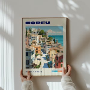 May include: A framed art print featuring a Mediterranean coastal town scene with the text CORFU at the top and the coordinates 39.6243 N, 19.9217 E at the bottom. The illustration depicts multi-colored buildings, a narrow street, and the sea.