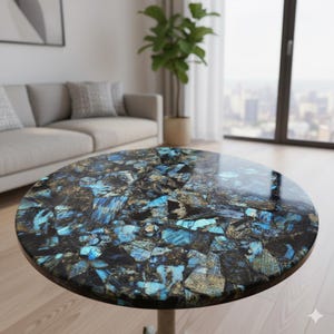 Puede incluir: Mesa de centro redonda con una superficie pulida en forma de mosaico. La tapa presenta un llamativo patrón de fragmentos azules, negros y dorados. La mesa tiene una sola base de pedestal de color claro, en un salón moderno.