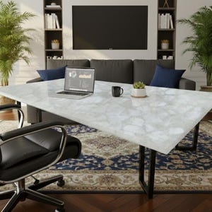 May include: A modern office setting featuring a large white marble-look table with black legs. A black office chair sits in front of the table, with a laptop, a black mug, and a small potted plant on top. A dark gray sofa and bookshelves are in the background.