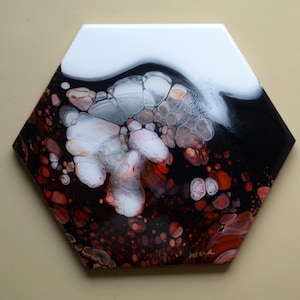 May include: Hexagon-shaped abstract art piece with a glossy finish. The artwork features a blend of white, black, and red hues, with a fluid, organic design. The piece is signed in the bottom right corner.