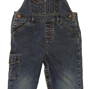 May include: Blue denim overalls with adjustable straps and multiple pockets. Features button closures on the sides and front. The overalls have a classic design with metal hardware and a faded wash.