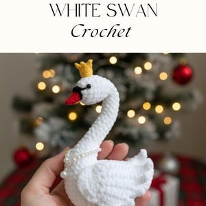 Puede incluir: Un cisne blanco de ganchillo con una corona amarilla, pico rojo y ojos negros. El cisne está adornado con un collar de perlas. El texto "WHITE SWAN Crochet" se muestra encima del cisne. El cisne se sostiene en una mano.