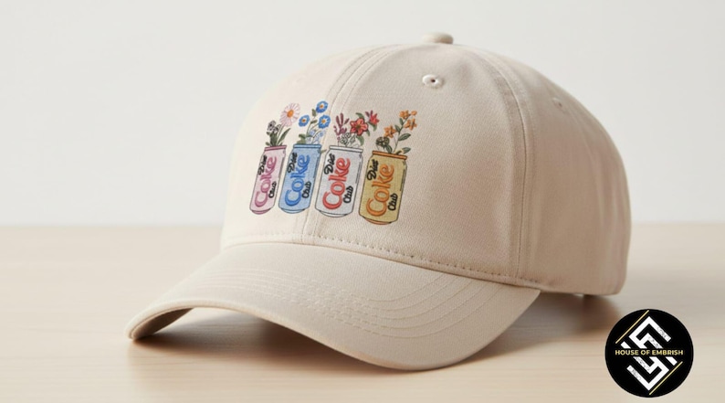 May include: A beige baseball cap featuring a colorful graphic of four Coke cans, each filled with different flowers. The cans are pink, blue, red, and yellow, with the word "Coke" printed on them. The cap has a curved brim.