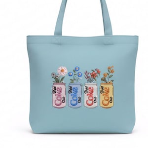 May include: Light blue tote bag featuring four embroidered soda cans, each holding a different arrangement of flowers. The cans are in pink, blue, red, and yellow, with the words "Coke" and "Diet Coke" on them.
