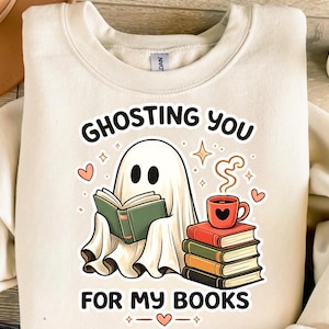 May include: A cream-colored crewneck sweatshirt featuring a graphic of a white ghost reading a green book. Next to the ghost is a stack of four books topped with a red mug. The text reads GHOSTING YOU FOR MY BOOKS, surrounded by small hearts and stars.