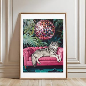 Könnte beinhalten: Gerahmter Kunstdruck mit einem grauen Wolf, der auf einem pinkfarbenen, getufteten Sofa liegt. Eine Discokugel hängt über dem Sofa vor einem Hintergrund aus tropischem Laub. Das Kunstwerk ist in einem goldfarbenen Rahmen.