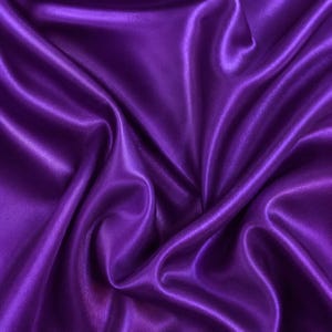 May include: A vibrant purple fabric with a smooth, lustrous finish and a reflective surface. The material is draped in soft, flowing folds that create deep shadows and bright highlights, emphasising the silky texture of the textile.