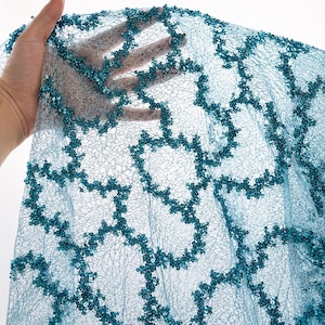 May include: A sheer light blue mesh fabric featuring an intricate, raised pattern of dark teal sequins arranged in organic, branching shapes. The delicate, web-like netting provides a translucent base for the dense, shimmering sequin embellishments.