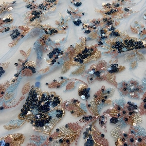 Può includere: Un tessuto a rete trasparente color azzurro con intricati ricami floreali. Il design è impreziosito da perline e paillettes blu navy scuro, oro metallizzato e oro rosa tenue, disposte in dettagliati motivi di fiori e foglie sulla superficie.