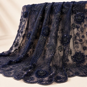 May include: A dark navy blue lace fabric featuring intricate floral embroidery, scattered sequins, and three-dimensional beaded flower appliqués. The sheer mesh material has a scalloped edge with detailed beadwork along the bottom border.