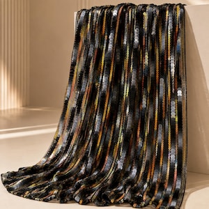 May include: A rectangular fabric runner featuring vertical stripes of shimmering black, gold, and iridescent sequins. The material is densely covered in small, reflective circular discs that create a textured, metallic appearance throughout the piece.