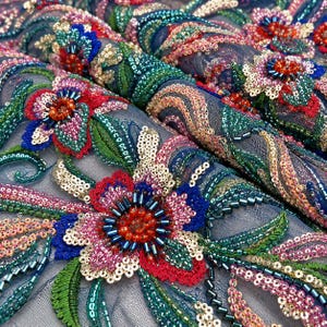 以下が含まれることがあります： 多色のスパンコールとガラスビーズで複雑な花の刺繍が施された、透明感のある青いメッシュ生地。赤、ピンク、青の花びら、緑の葉のアクセント、そして半透明のベースに金色のスパンコールの渦巻き模様がデザインされています。