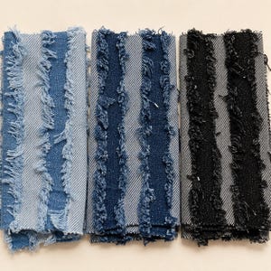 May include: Three rectangular fabric swatches featuring a vertical striped pattern with frayed, raw edges. The left swatch is light blue, the center swatch is medium blue, and the right swatch is black, all displaying a distinct diagonal twill weave.