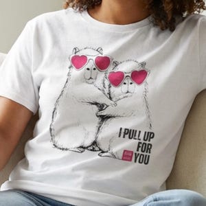 May include: White t-shirt featuring a graphic of two cartoon bears wearing heart-shaped sunglasses, embracing. The text "I pull up for you" is printed below the bears in black and pink. The shirt is worn by a person.