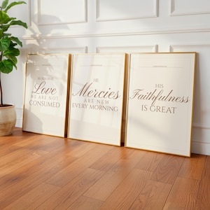 Può includere: Tre stampe artistiche incorniciate con bordi dorati e sfondi color crema. Ogni stampa presenta un'elegante tipografia con frasi come "Amore, non siamo consumati" e "Le sue misericordie sono nuove ogni mattina."