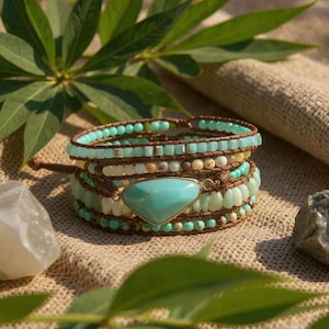 Puede incluir: Pulsera envolvente con cuentas turquesas y verde claro, con una gran piedra turquesa. La pulsera está hecha con cuero marrón y tiene un estilo bohemio. La pulsera se muestra sobre una superficie de color neutro.