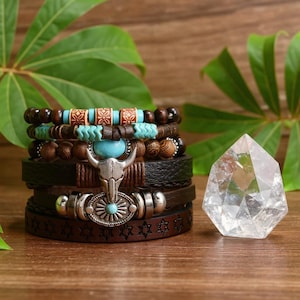 Könnte beinhalten: Ein Stapel Armbänder im Bohème-Stil mit Leder, Holzperlen und türkisfarbenen Akzenten. Die Armbänder haben einen silbernen Bullenschädel-Anhänger und ein Lederband mit Sternmuster. Rechts befindet sich ein klarer Kristall.