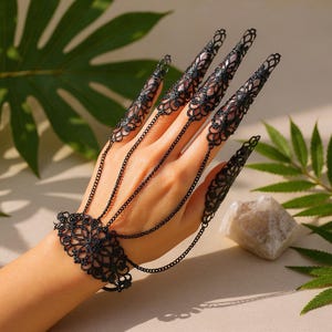 Può includere: Armatura per dita in filigrana nera con dettagli a catena. I gioielli in stile gotico presentano intricati disegni a pizzo sulle punte delle dita e un braccialetto abbinato. Il set è collegato da delicate catene.