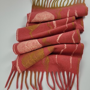 Könnte beinhalten: Handgefertigter Filzschal in Rottönen mit goldenen und cremefarbenen Akzenten. Der Schal hat einen Fransenrand und dekorative Muster. Das Design umfasst kreisförmige und lineare Elemente, die ein einzigartiges Accessoire schaffen.