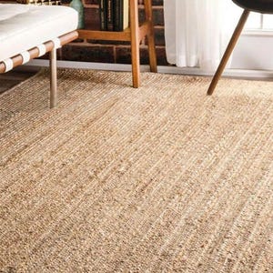 Könnte beinhalten: Ein rechteckiger Teppich aus Naturfasern mit gewebter Textur. Der Teppich hat eine hellbraune Farbe, möglicherweise Jute oder ein ähnliches Material. Er bedeckt eine große Fläche des Bodens.