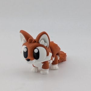 Peut inclure: Une petite figurine de renard articul&eacute;e pr&eacute;sentant un corps orange vif avec des accents blancs sur la poitrine, les pattes et l'int&eacute;rieur des oreilles. Le renard a de grands yeux noirs ronds et un petit nez noir, avec des lignes d'impression 3D visibles.