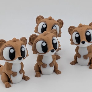 May include: Several brown and white cartoon squirrel figurines with large, expressive eyes are arranged on a white surface. The figurines have a 3D printed appearance and are posed in various positions, showcasing their detailed design.