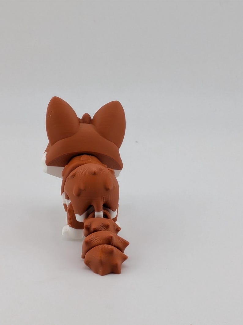 Peut inclure: Une petite figurine de renard articul&eacute;e avec une finition mate dans des tons brun-rouge et blanc. Le renard est repr&eacute;sent&eacute; de dos, mettant en valeur ses oreilles pointues, son dos textur&eacute; et sa queue segment&eacute;e et flexible.