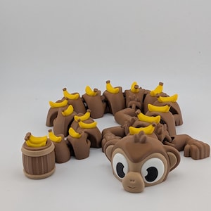 May include: Brown monkey-themed decorative items with yellow bananas. The collection includes a barrel, monkey heads, and monkey body parts. The monkey heads have large white eyes and a smiling expression. The bananas are a bright yellow color.