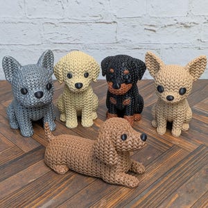 May include: A collection of five dog figurines with a textured, knit-like surface. The group includes a grey French Bulldog, a cream-colored dog, a black and tan dog, a tan Chihuahua, and a brown Dachshund lying in the front center.