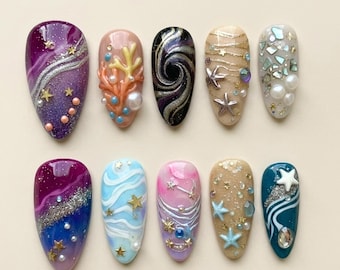 Puede incluir: Un conjunto de diez uñas postizas en forma de almendra con diseños variados que incluyen purpurina morada, texturas de coral, espirales negras, estrellas de mar, perlas, fragmentos de concha iridiscentes y estrellas doradas en varias paletas.