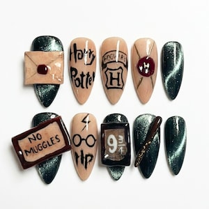 Puede incluir: Un juego de diez uñas postizas con una mezcla de esmalte verde oscuro efecto ojo de gato y uñas color nude con diseños pintados a mano que incluyen una carta, el texto Harry Potter, el escudo de Hogwarts, gafas, un rayo, No Muggles, 9 3/4 y una varita.