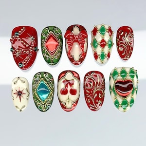 May include: A set of ten press-on nails featuring festive designs in red, green, cream, and gold. The nails display intricate patterns including raised bows, cherries, hearts, diamond grids, and starbursts with metallic gold detailing and glossy finishes.